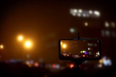 Image of Taking photo of with smartphone mounted on tripod. Blurred view of city lights at night, bokeh effect
