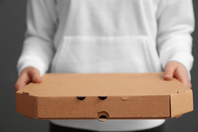 Photo of Young woman with pizza box on grey background, closeup. Food delivery service