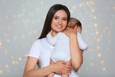 Photo of Young mother holding her adorable baby against defocused lights