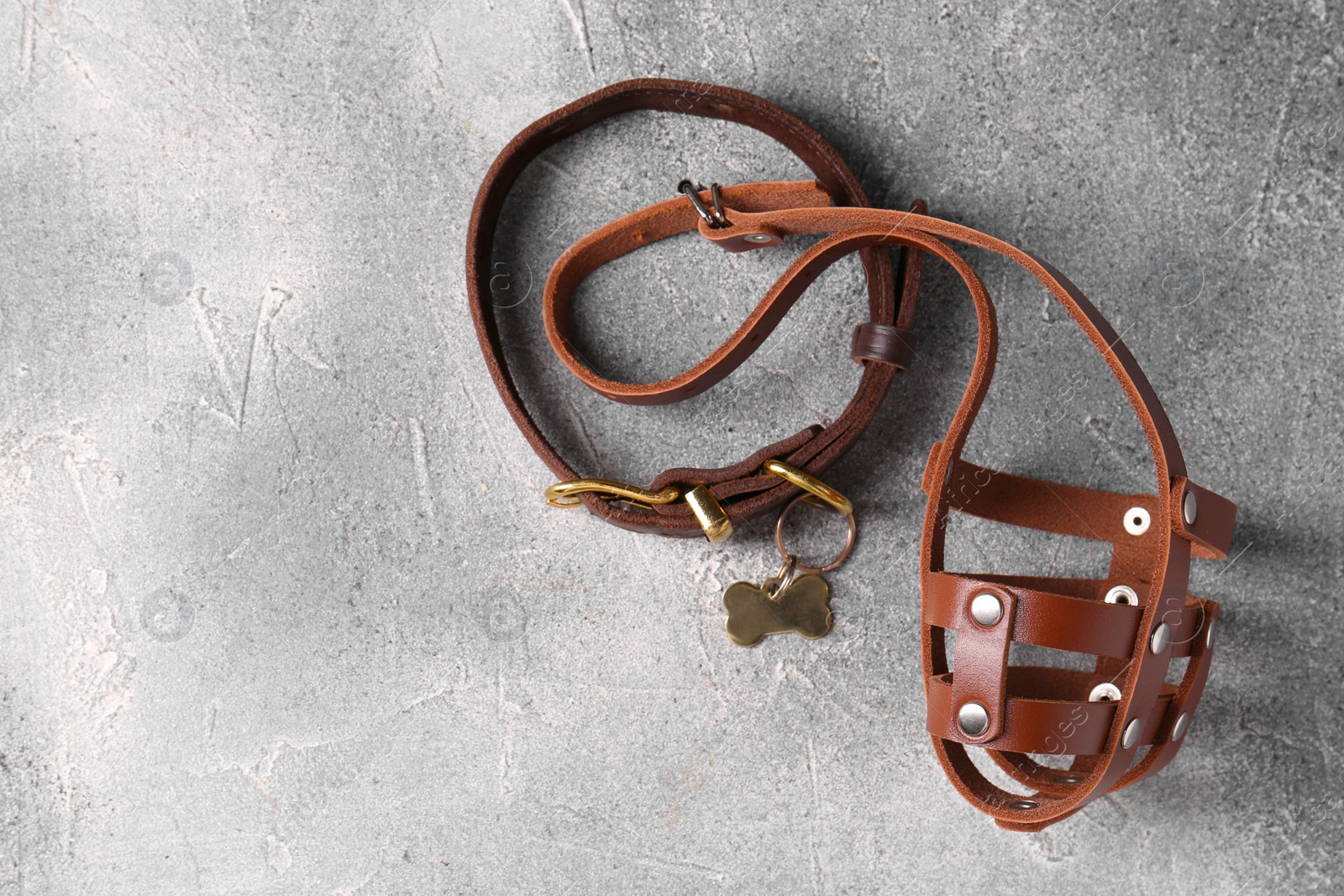 Photo of Brown leather dog muzzle and collar on light gray textured table, top view. Space for text