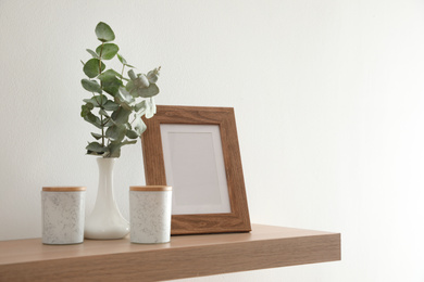 Photo of Wooden shelf with photo frame and decorative elements on light wall