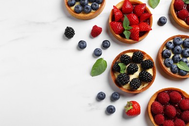 Photo of Tartlets with different fresh berries on white marble table, flat lay and space for text. Delicious dessert