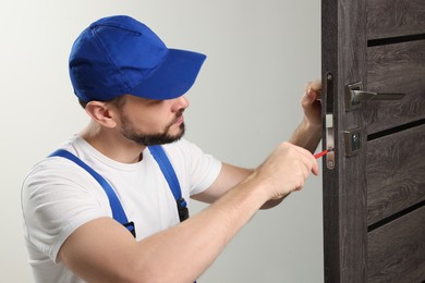 Photo of Worker in uniform with screwdriver repairing door lock indoors