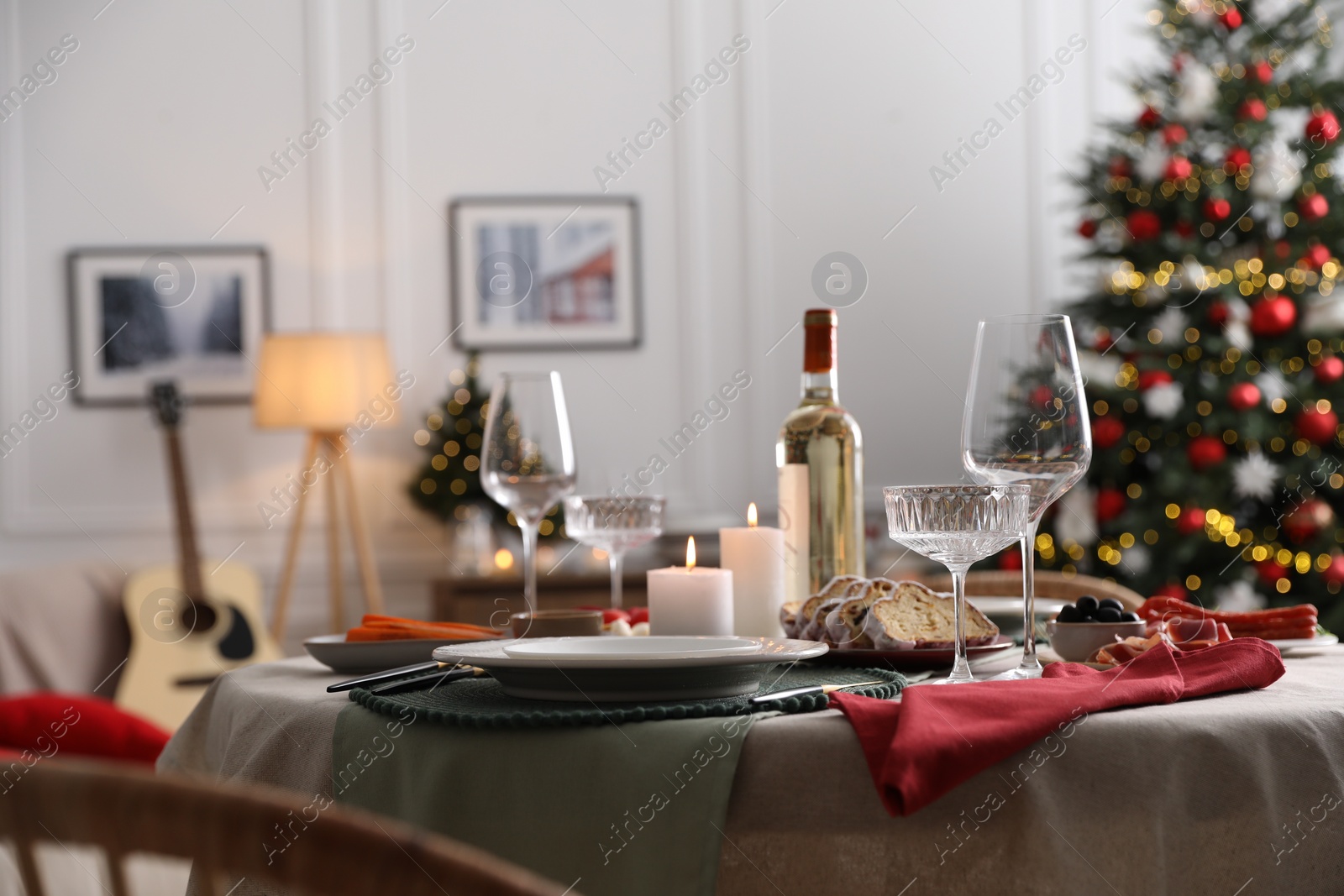 Photo of Christmas table setting with burning candles, appetizers and dishware in room