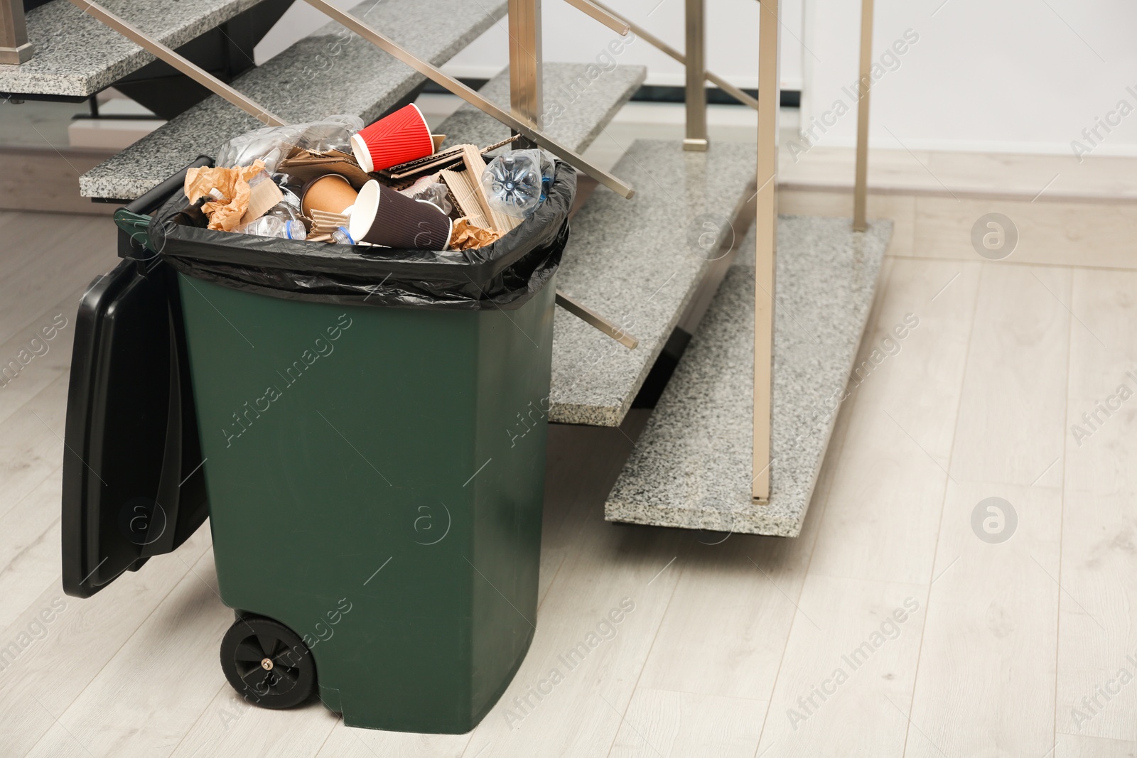 Photo of Full trash bin near stair way indoors. Waste recycling