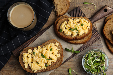 Photo of Tasty scrambled egg sandwiches served on wooden table, flat lay