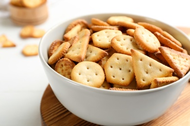 Photo of Delicious crispy crackers in bowl on white table, closeup