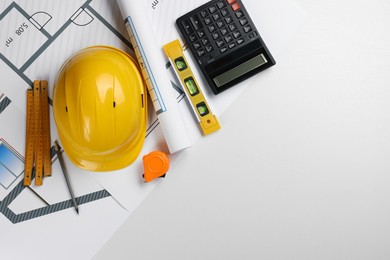 Photo of Construction drawings, safety hat, calculator, tape measure, folding ruler and bubble level on white background, top view. Space for text