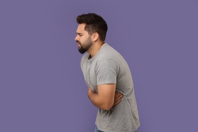 Young man suffering from stomach pain on purple background