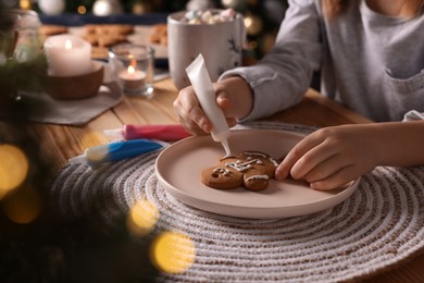 Photo of Little child decorating Christmas cookie at wooden table, closeup