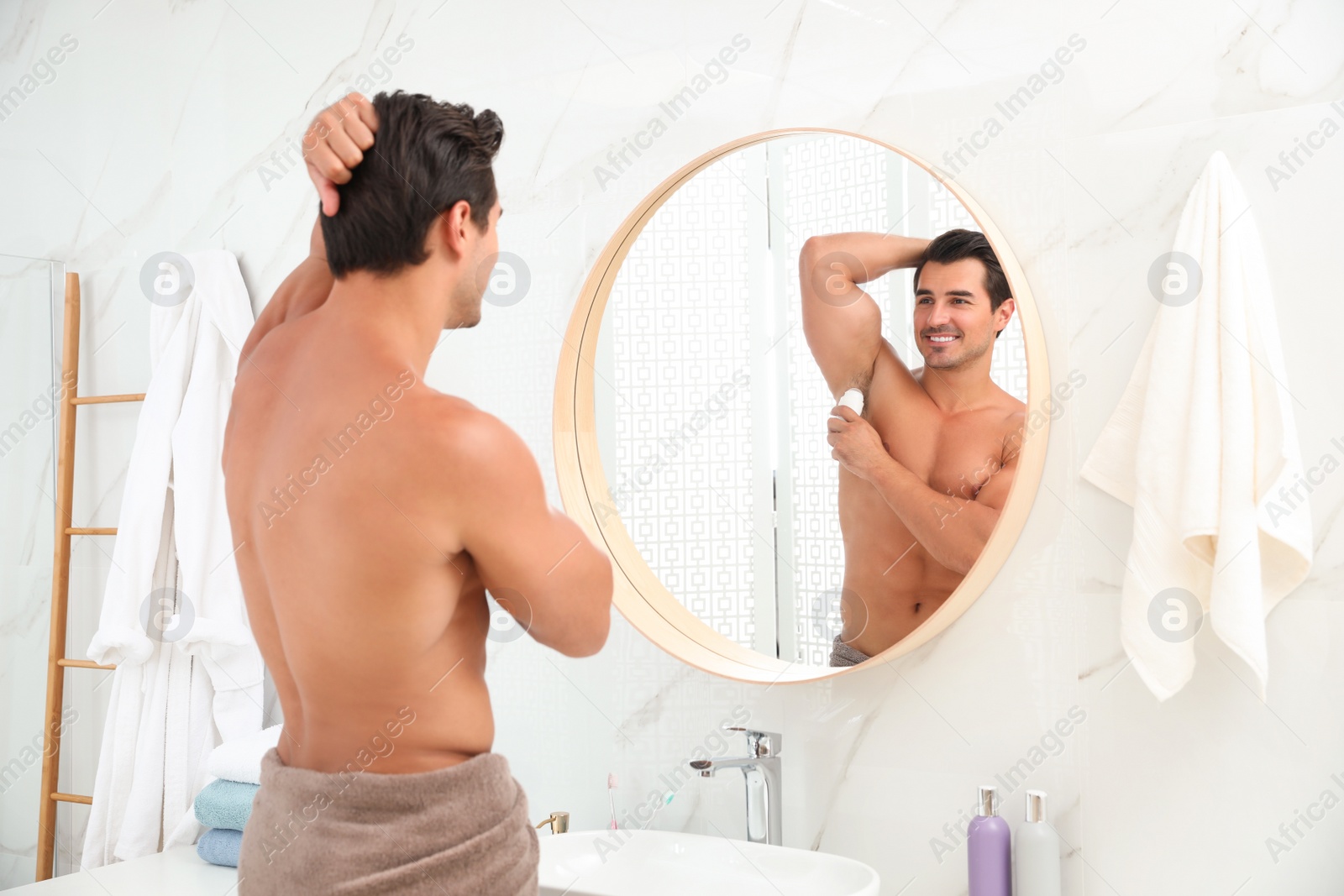 Photo of Handsome young man applying deodorant in bathroom