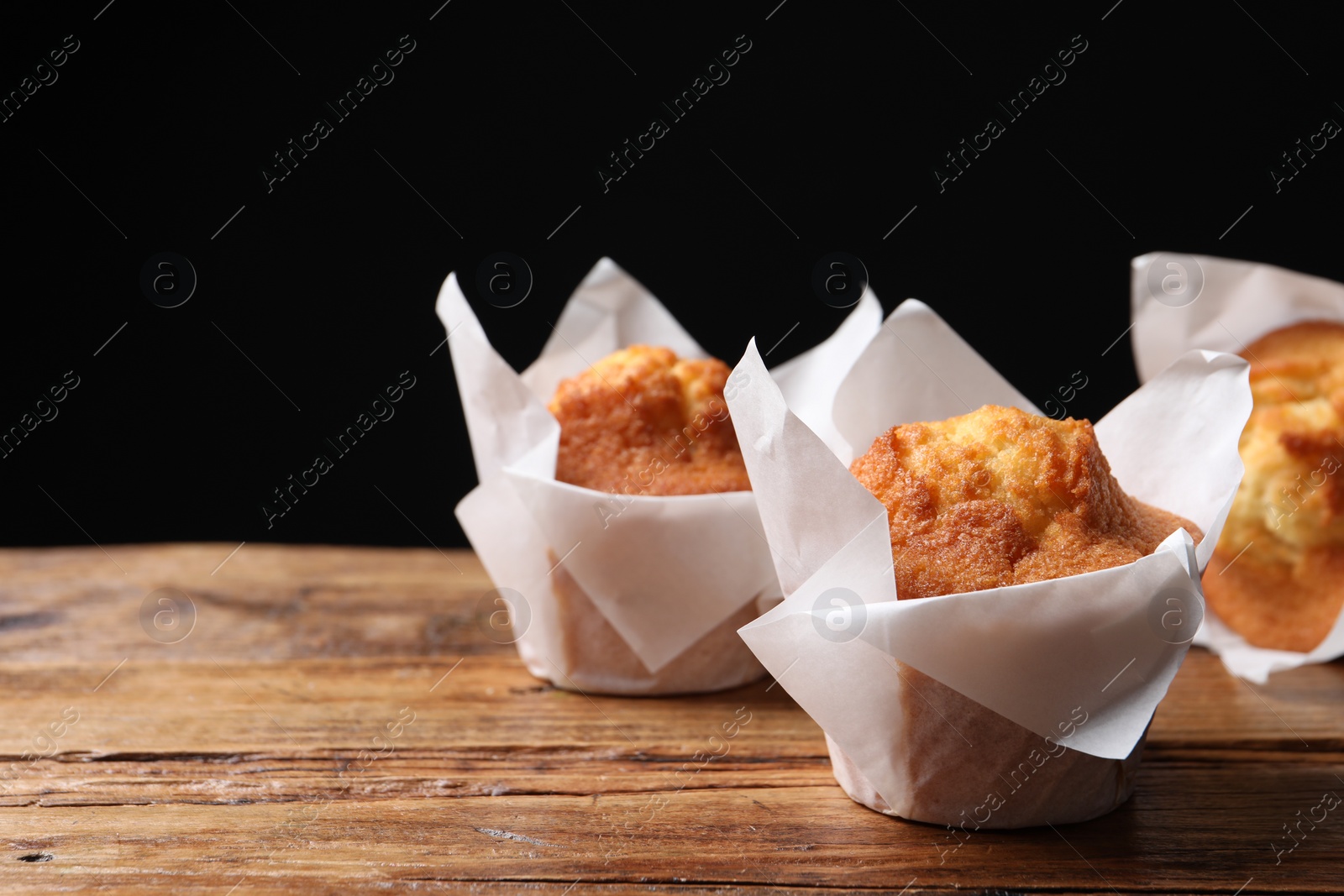 Photo of Delicious sweet muffins on wooden table against dark background, closeup. Space for text