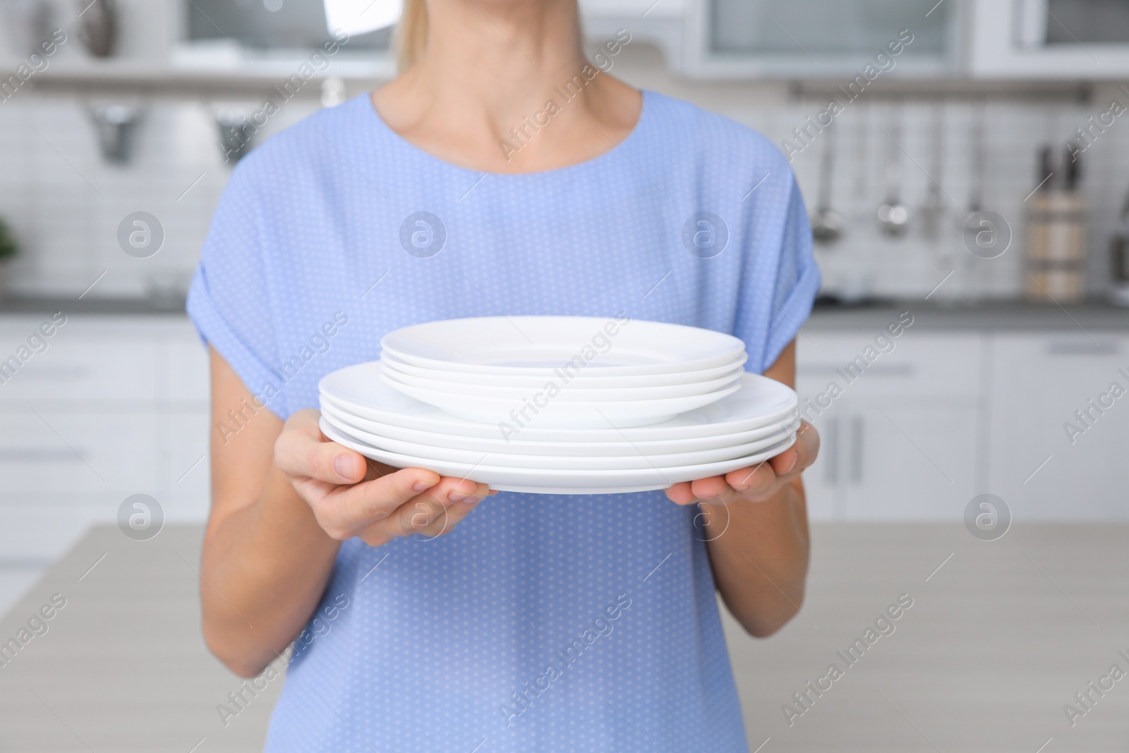 Photo of Woman with stack of clean dishes in kitchen, closeup