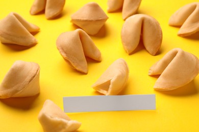 Photo of Many tasty fortune cookies with predictions on yellow background, closeup. Space for text