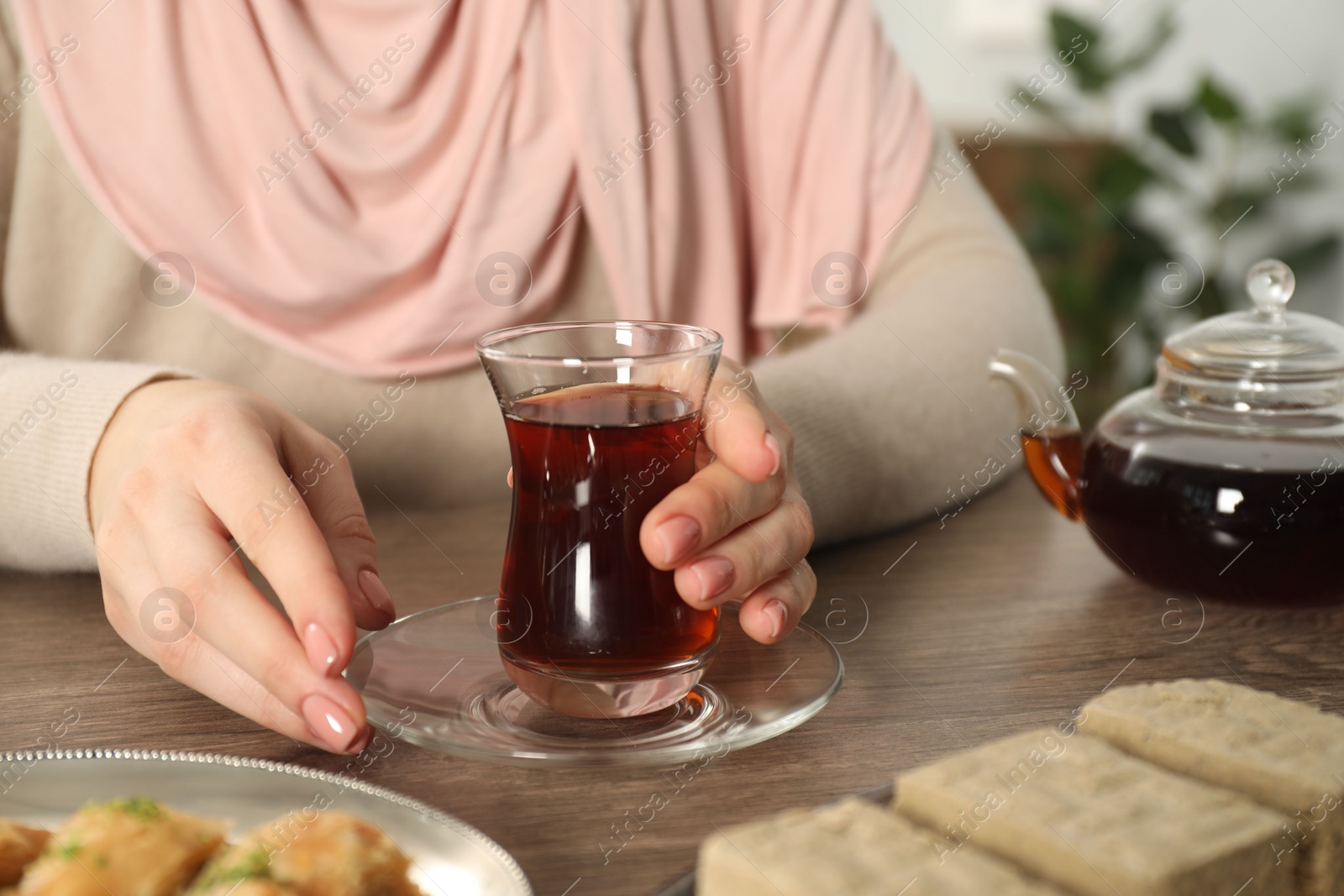 Photo of Woman with cup of delicious Turkish tea at wooden table, closeup