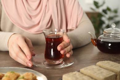 Photo of Woman with cup of delicious Turkish tea at wooden table, closeup