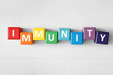 Photo of Colorful cubes with word Immunity on white wooden table, flat lay