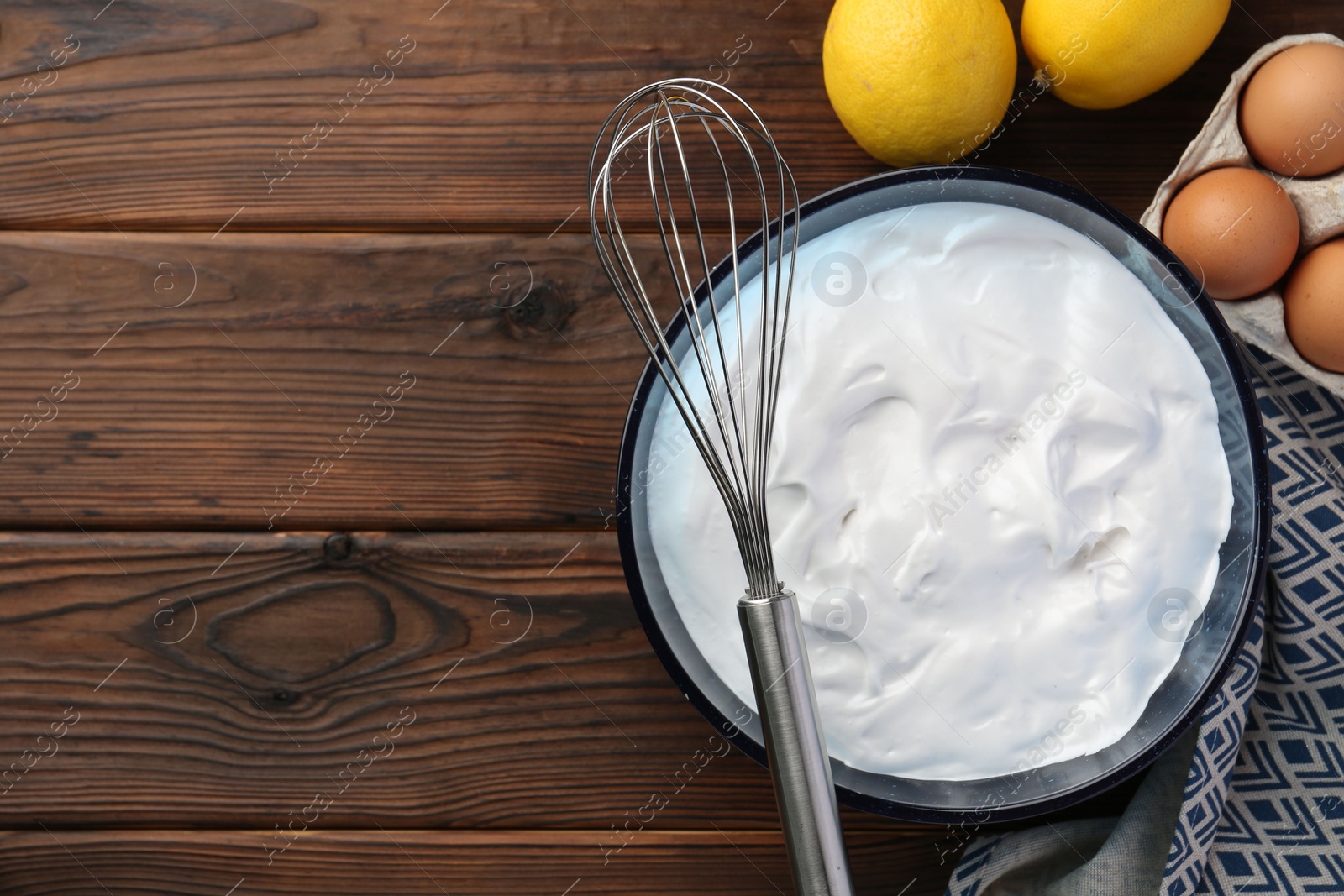 Photo of Bowl with whipped cream, whisk and ingredients on wooden table, flat lay. Space for text