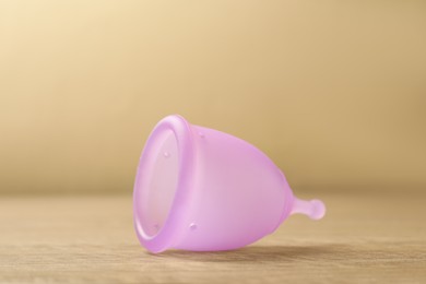 Photo of Menstrual cup on wooden table, closeup. Reusable female hygiene product