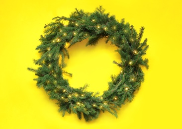 Photo of Beautiful Christmas wreath with festive lights on yellow background, top view