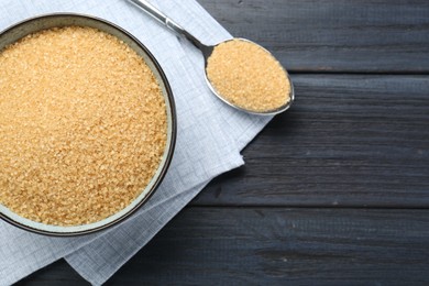 Photo of Brown sugar in bowl and spoon on black wooden table, flat lay. Space for text