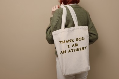 Image of Woman holding bag with phrase Thank God I Am Atheist on beige background, closeup