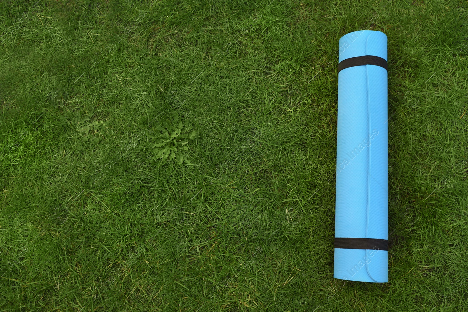 Photo of Bright karemat or fitness mat on fresh green grass outdoors, top view. Space for text