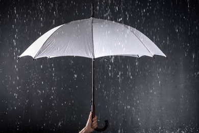 Photo of Woman holding white umbrella under rain on dark background, closeup