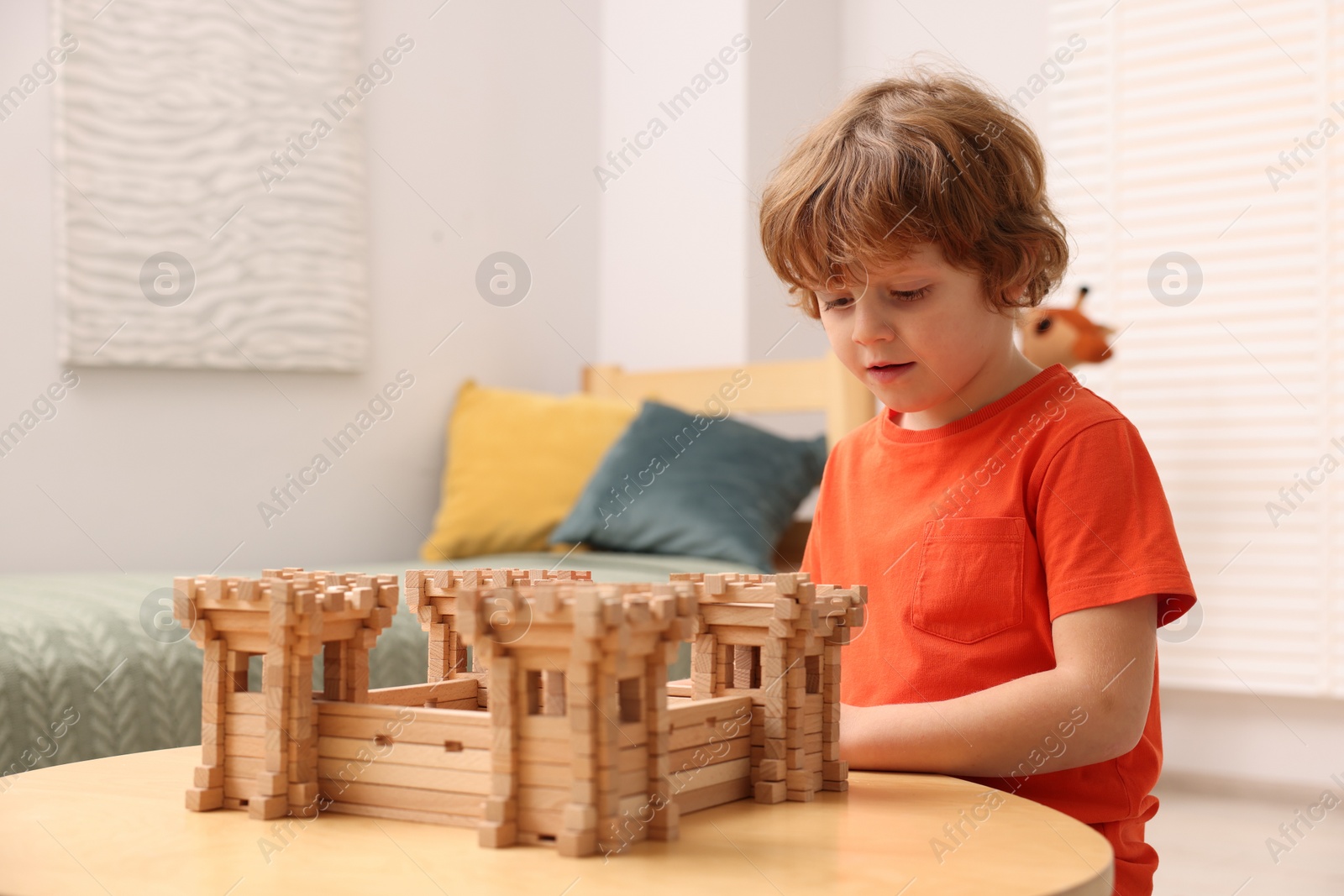 Photo of Cute little boy playing with wooden fortress at table in room. Child's toy