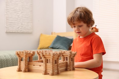 Cute little boy playing with wooden fortress at table in room. Child's toy