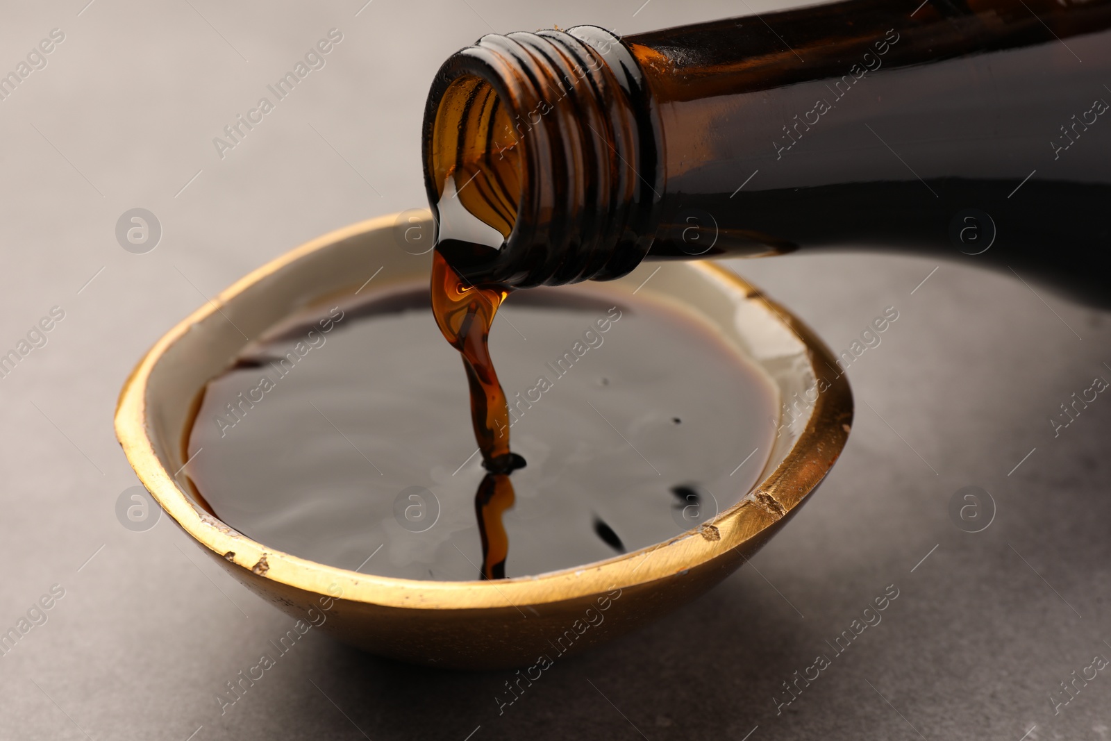 Photo of Pouring soy sauce into bowl on grey table, closeup