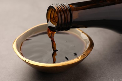 Pouring soy sauce into bowl on grey table, closeup