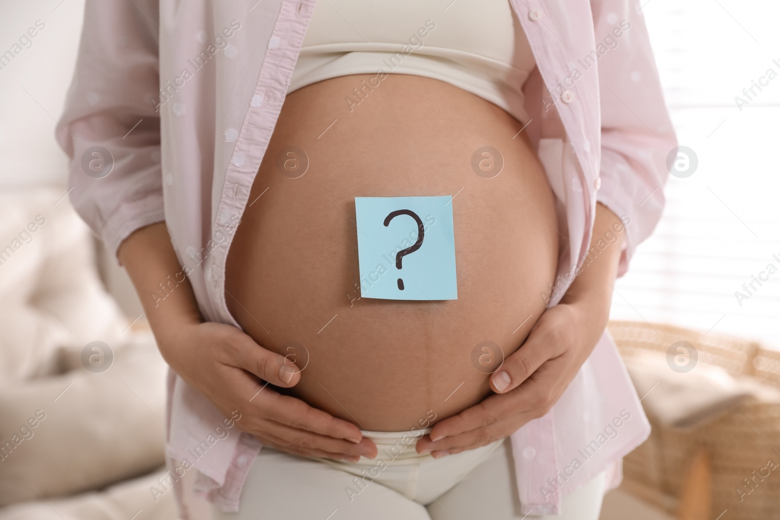 Photo of Pregnant woman with sticky note on belly indoors, closeup. Choosing baby name