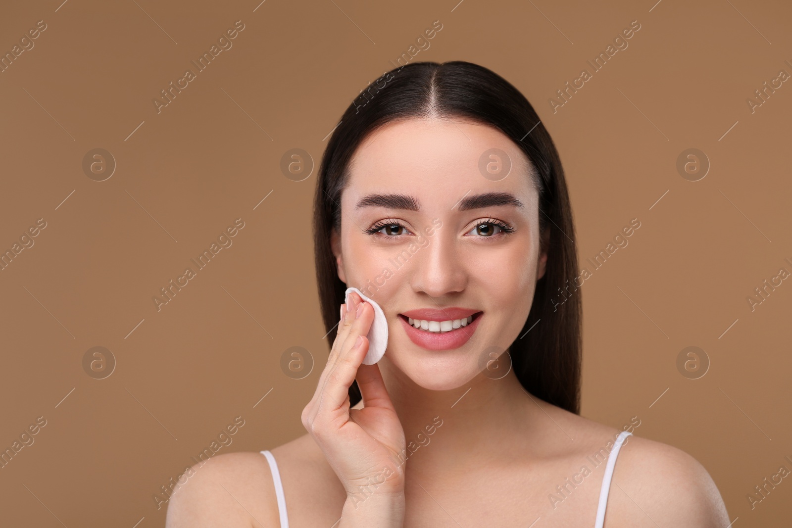 Photo of Beautiful woman removing makeup with cotton pad on beige background