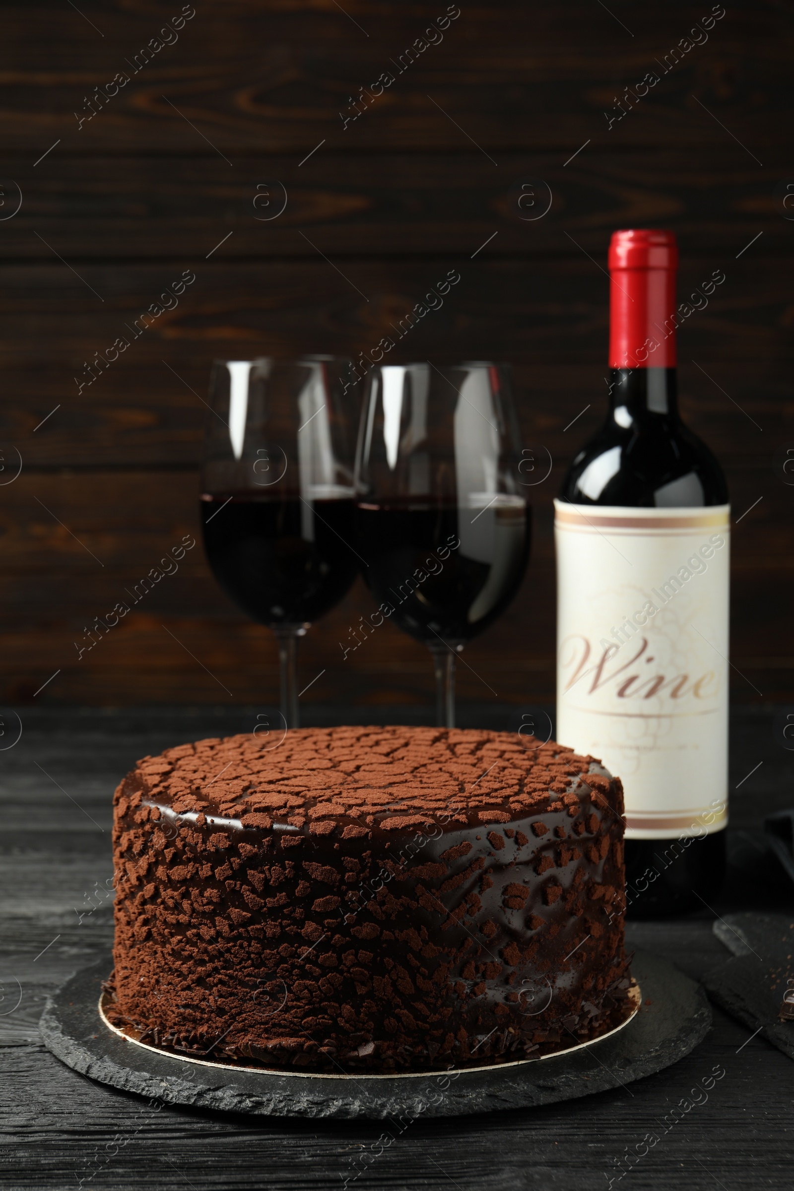 Photo of Delicious chocolate truffle cake and red wine on black wooden table