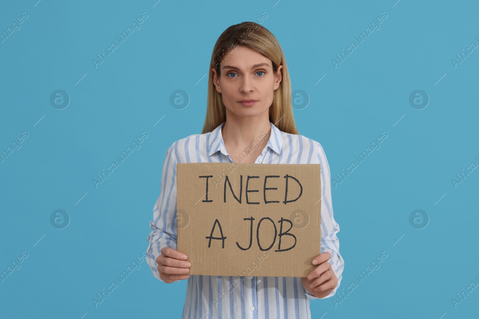 Photo of Unemployed woman holding sign with phrase I Need A job on light blue background