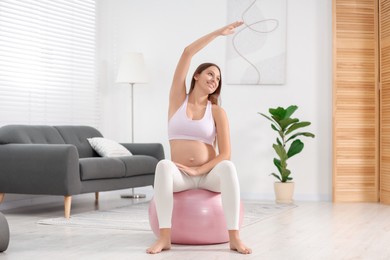 Photo of Pregnant woman doing exercises on fitness ball in room. Home yoga