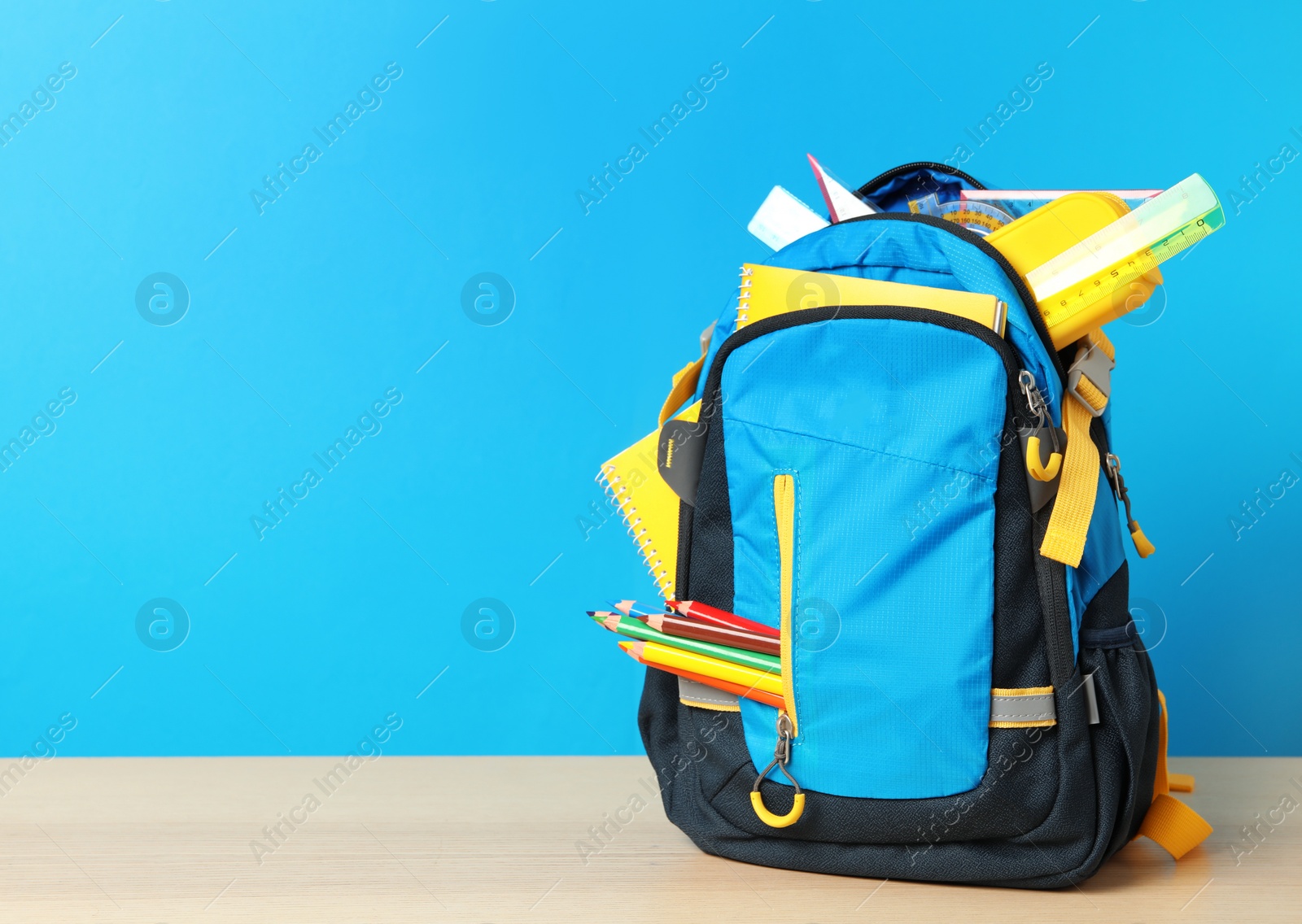 Photo of Stylish backpack with different school stationery on wooden table against light blue background, space for text. Back to school