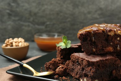 Delicious chocolate brownies with nuts, caramel sauce and fresh mint on plate, closeup