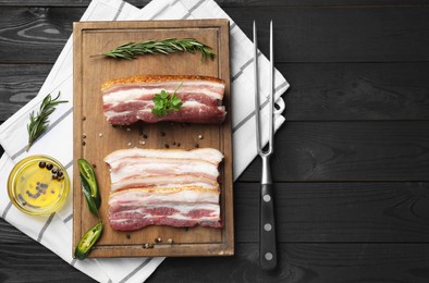 Photo of Pieces of raw pork belly, chili pepper, peppercorns, rosemary and parsley on black wooden table, flat lay