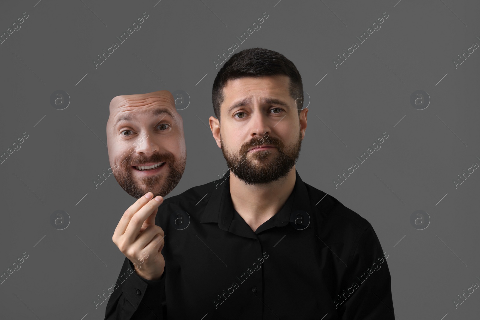 Image of Man holding mask with his facial expression on grey background. Personality crisis, different emotions