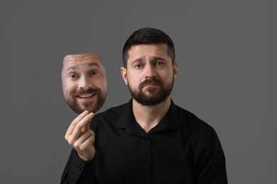 Image of Man holding mask with his facial expression on grey background. Personality crisis, different emotions