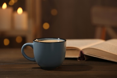 Cup of hot coffee and book on wooden table in room