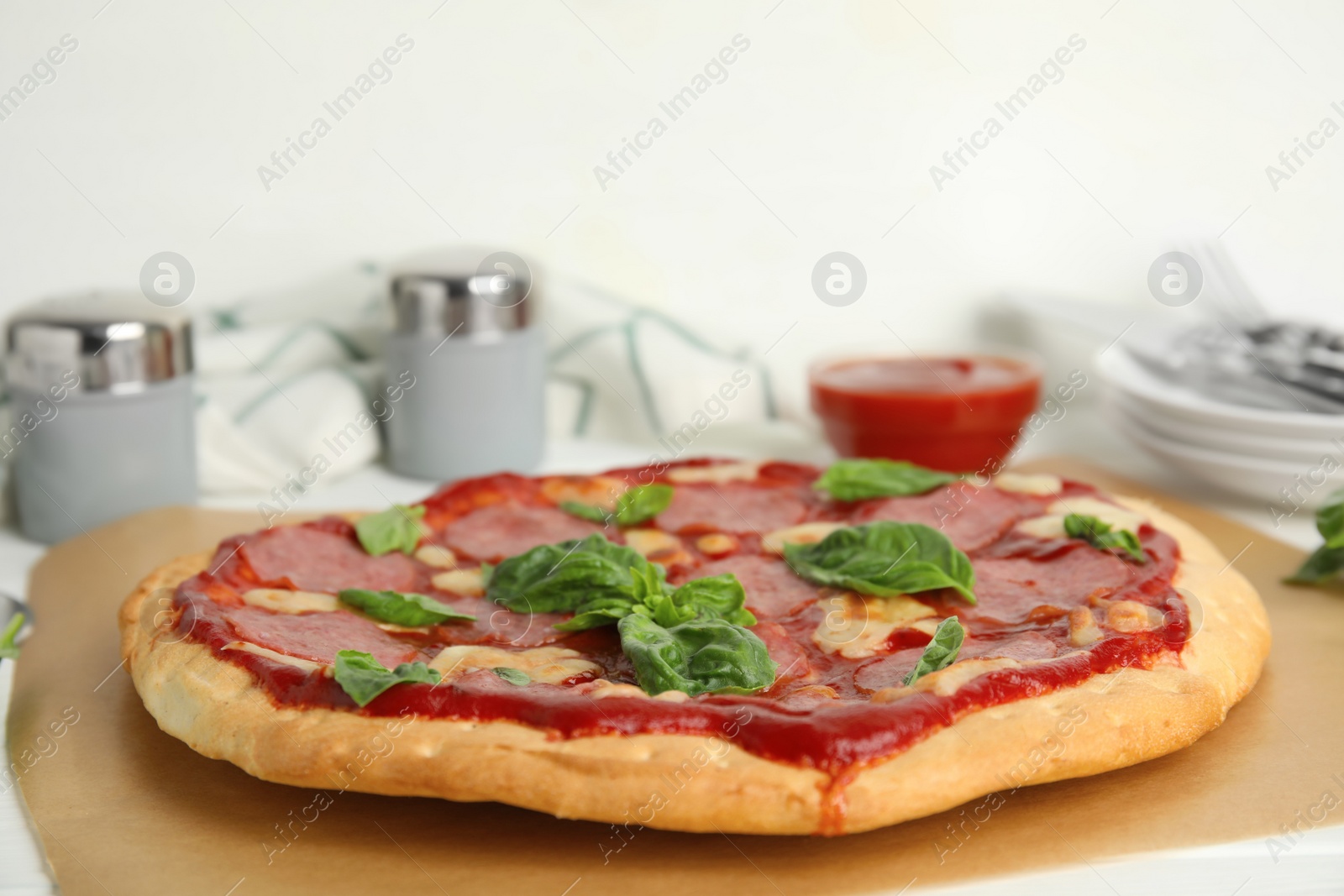 Photo of Pita pizza with pepperoni, cheese and basil on parchment, closeup