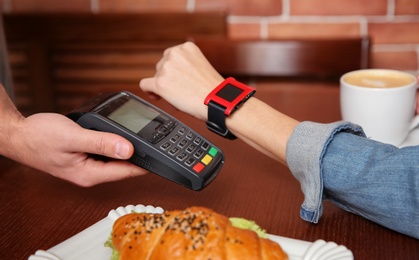 Woman using terminal for contactless payment with smart watch in cafe, closeup