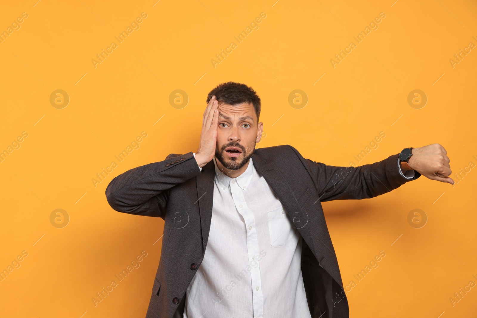 Photo of Emotional man showing time on watch against orange background. Being late concept