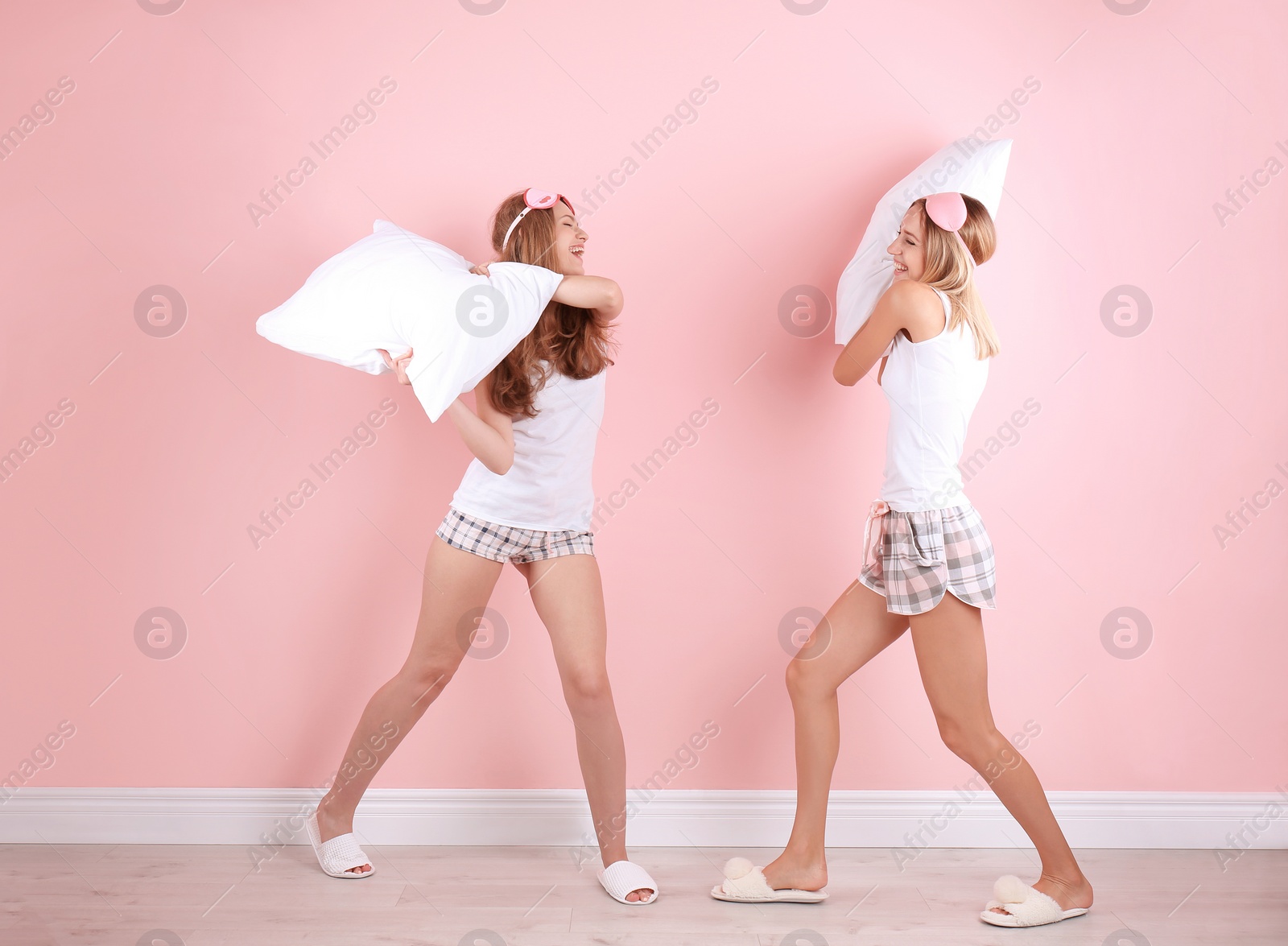 Photo of Two young women having pillow fight near color wall