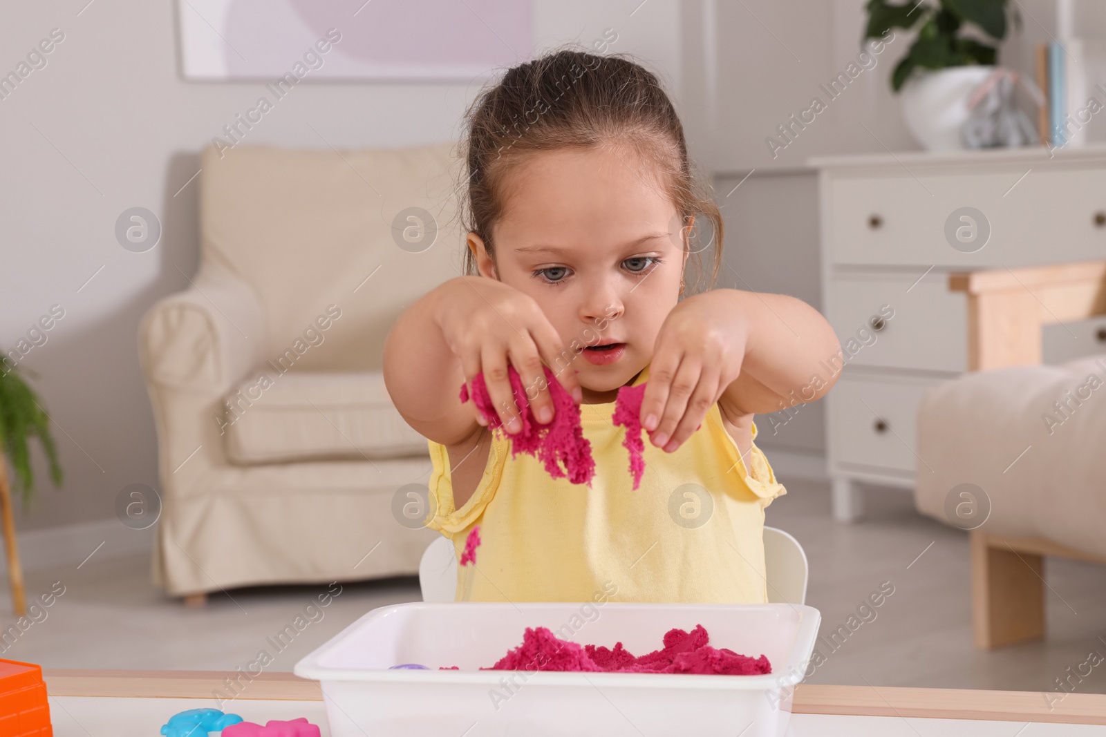 Photo of Cute little girl playing with bright kinetic sand at table in room