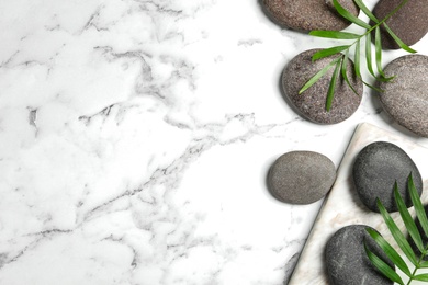 Photo of Spa stones and green leaves on white marble table, flat lay. Space for text