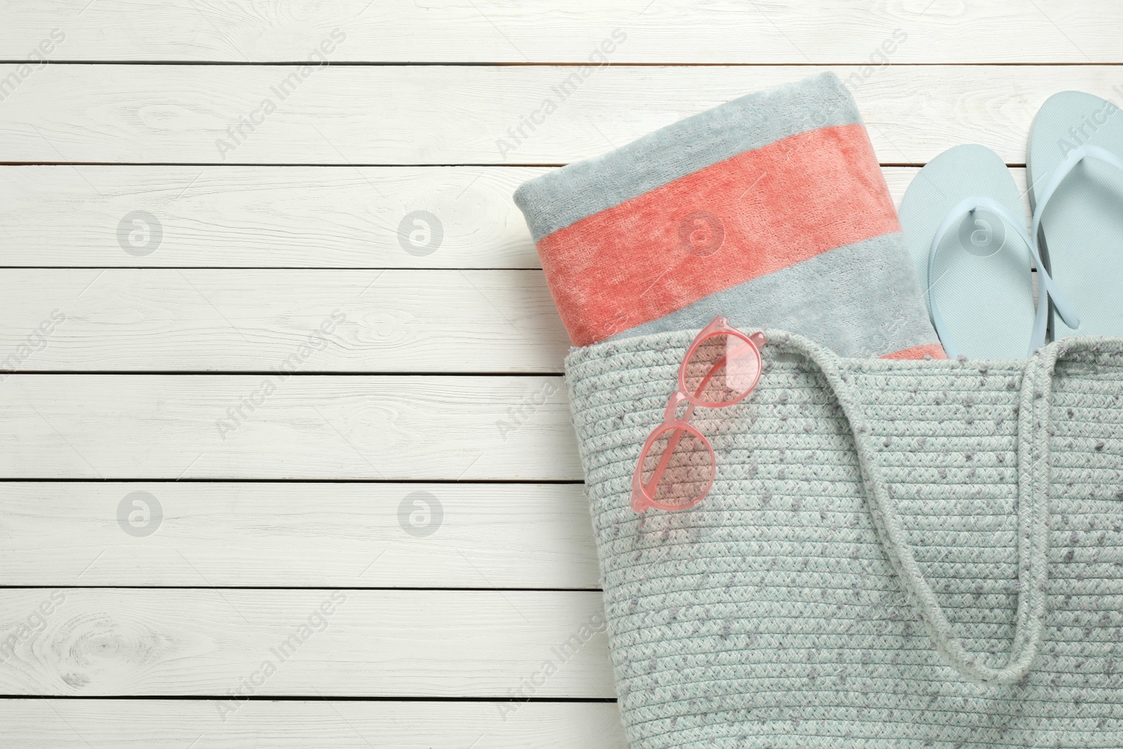 Photo of Beach bag with towel, flip flops and sunglasses on white wooden background, flat lay. Space for text